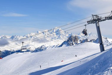 Les Menuires sandalyesinin nefes kesen manzarası üç vadideki karlı dağların üzerinden yükseliyor. Tarentaise Vadisi bölgesindeki Fransız kayak merkezinde kayakçılar ve snowboardcular..