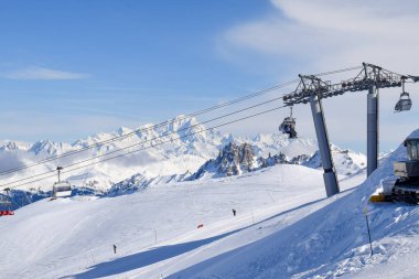 Les Menuires sandalyesinin nefes kesen manzarası üç vadideki karlı dağların üzerinden yükseliyor. Tarentaise Vadisi bölgesindeki Fransız kayak merkezinde kayakçılar ve snowboardcular..