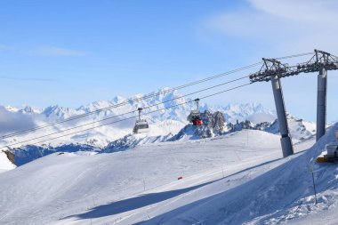 Les Menuires sandalyesinin nefes kesen manzarası üç vadideki karlı dağların üzerinden yükseliyor. Tarentaise Vadisi bölgesindeki Fransız kayak merkezinde kayakçılar ve snowboardcular..