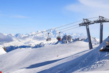 Les Menuires sandalyesinin nefes kesen manzarası üç vadideki karlı dağların üzerinden yükseliyor. Tarentaise Vadisi bölgesindeki Fransız kayak merkezinde kayakçılar ve snowboardcular..