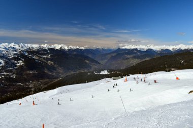 Fransa 'nın Üç Vadisi' ndeki popüler kayak merkezi Meribel 'den bir dağ vadisi manzarası. Kayakçılar ve snowboardcular soluk kesen Fransız Alp Dağları 'nın arka planında piste çıkıyorlar..
