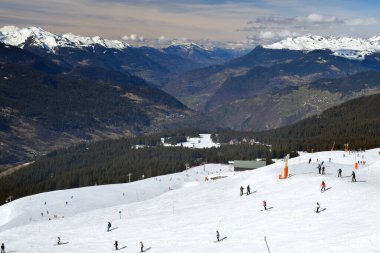 Fransa 'nın Üç Vadisi' ndeki popüler kayak merkezi Meribel 'den bir dağ vadisi manzarası. Kayakçılar ve snowboardcular soluk kesen Fransız Alp Dağları 'nın arka planında piste çıkıyorlar..