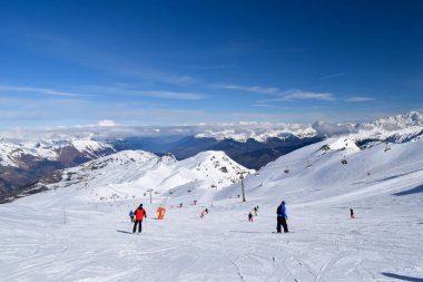 Kayakçılar ve snowboardcular Les Menuires kayak merkezindeki karlı pistlerde yokuş aşağı gidiyorlar. Üç vadideki karlı Fransız dağlarının zirvelerine bakan kış sporları aktiviteleri.