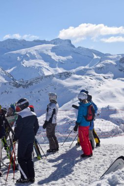 Meribel, Fransa - 13 Mart 2024: Fransa 'nın Üç Vadisi' ndeki Meribel kayak merkezinin tepesindeki dağ manzarasına bakan kayakçılar ve snowboardcular grubu.