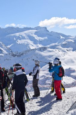 Meribel, Fransa - 13 Mart 2024: Fransa 'nın Üç Vadisi' ndeki Meribel kayak merkezinin tepesindeki dağ manzarasına bakan kayakçılar ve snowboardcular grubu.
