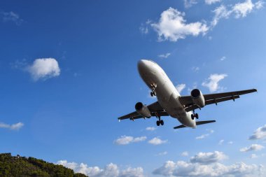 Alttan uçan büyük bir uçak görünüyor. İniş için hazırlanan ticari bir uçağın altından etkileyici bir açı. Parlak mavi gökyüzüne doğru uçan bir uçağın yakınında.