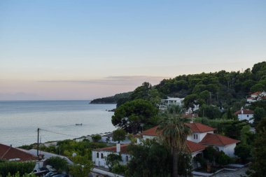Yunanistan 'ın Skiathos Adası' ndan Akdeniz üzerinde gün batımı. Yemyeşil ağaçlar Yunan ada manzarasını kaplıyor ve kıyı şeridi sıcak bir yaz akşamında sakin bir okyanusla karşılaşıyor. 
