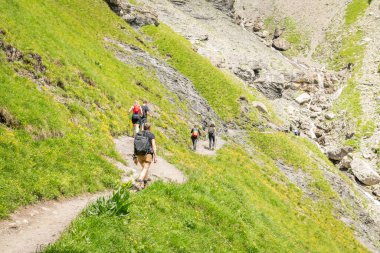 Hikers on a trail in the Swiss mountains around Oeschinensee. Hiking trail high up in the mountains. Sunny summer day in the Swiss Alps. Alpine meadow, high mountains. 5 july 2024, Oeschinensee. clipart