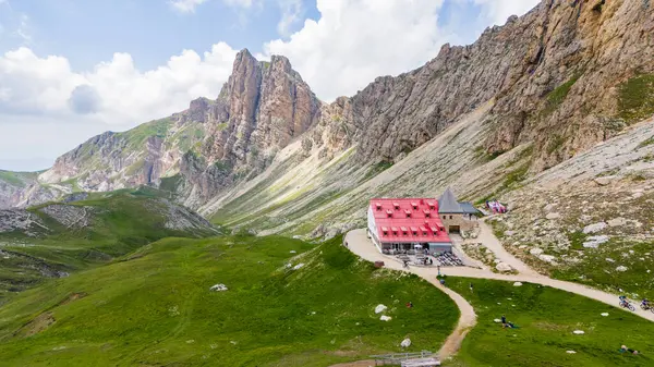 Yaz boyunca Tierser Alpl dağ kulübesinin (Rifugio Alpe di Lastikleri) insansız hava aracı görüntüsü. Terralardaki bazı insanlar. Ön planda taze yeşil çayır, arka planda görkemli dağlar..