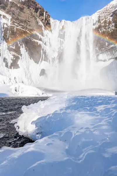 stock image View of the famous Skgafoss ( Skogafoss) waterfall during winter in the south of Iceland near Skogar town. Amazing cascade with ice and snow and partially frozen river.