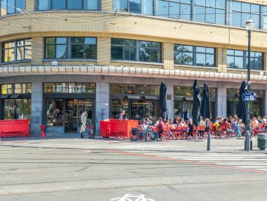 20 september 2024, Elsene, Belgium. People on terras at Flagey square taken a break, drinking and enjoying good weather in september. Pause during the day. Part of old Belgian radio and television T building in the background. clipart