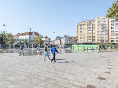 20 Eylül 2024, Elsene, Belçika. Bazı insanlar, erkek ve kadın Flagey meydanında yürüyorlar. Su çeşmesi güneşli bir günde su püskürtür. Konut binaları. Flagey Meydanı.