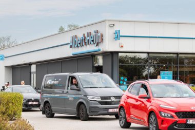 22 Eylül 2024, Genk, Belçika. Albert Heijn mağazasının önünde yürüyen insanlar var. Ön cephede markalı bir tabela. İnsanlar otoparkta yürüyorlar. Otoparktaki müşteriler