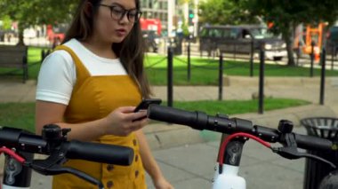 4K Asyalı Kadın Elektrikli Scooter Sürüşü için Akıllı Telefon Uygulaması Kullanıyor