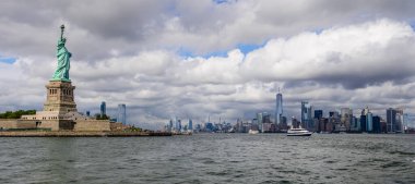 New York şehrinin arka planında bulutlu bir günde Özgürlük Heykeli ve Manhattan.