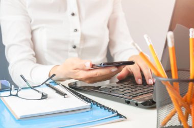 İş yerinde akıllı telefon ve laptop kullanan bir kadın.