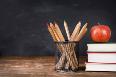 Masanın üzerinde karatahta arka planına karşı kitap, elma ve kalem yığını, boşluk kopyala