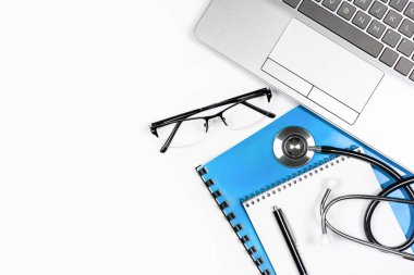 Beyaz arkaplanda kalem ve gözlüklü, steteskop ve dizüstü bilgisayarı olan not defteri, kopya alanı olan üst görünüm