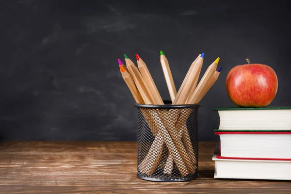 Masanın üzerinde karatahta arka planına karşı kitap, elma ve kalem yığını, boşluk kopyala