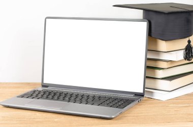 Mezuniyet şapkalı kitap yığınının yanında boş ekran dizüstü bilgisayar. E-öğrenme ve çevrimiçi mezuniyet kavramı