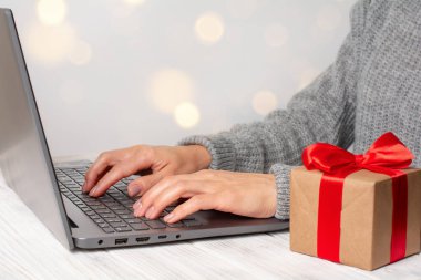 Dizüstü bilgisayar kullanan kadın eller, masadaki dizüstü bilgisayarın yanında hediye kutusu. Çevrimiçi Noel alışveriş kavramı