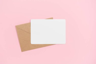 Pembe zemin üzerinde el işi zarfı olan boş beyaz kart, boşluğu kopyala