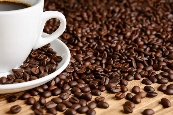 Kahve çekirdekleri ve kahve fincanı ahşap masada.