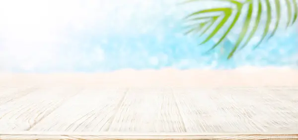 Bulanık mavi parlak deniz arka planı ve palmiye yaprağı üzerindeki beyaz ahşap masa.