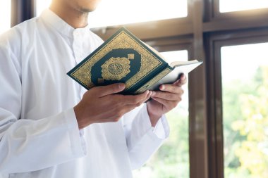 Muslim man reading holy Quran. Holy Quran in Hand with arabic text meaning of Al Quran clipart