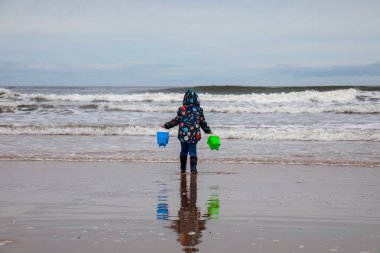 Genç bir çocuk sahilde yürür sahilde kovaları suyla doldurmak için
