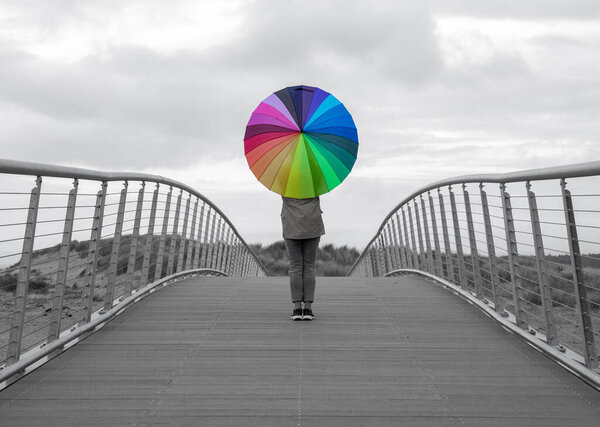 Одинокая девушка стоит на мосту с радужным зонтиком