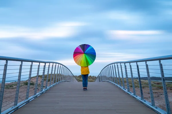 stock image lone girl standing on bridge with rainbow umbrella