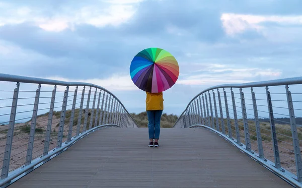 Stock image Lone girl standing on bridge with rainbow umbrella