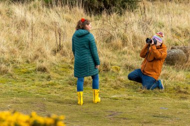 man taking a photograph of his girlfriend on holiday and she has lovely bright yellow wellington boots clipart