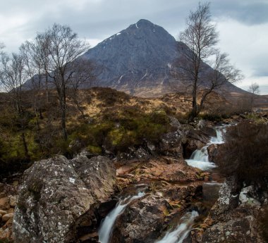 Buachaille Etive Mor, Glencoe 'daki Glen Etive ve altında şelale olan ikonik bir İskoç dağı. Ünlü bir manzarası ve baharda İskoçya manzarası olan, fırtınalı bir gökyüzü ve çağlayan ağaçlarla dolu bir suyu olan bir yer.