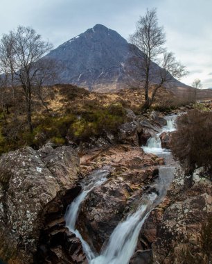 Buachaille Etive Mor, Glencoe 'daki Glen Etive ve altında şelale olan ikonik bir İskoç dağı. Ünlü bir manzarası ve baharda İskoçya manzarası olan, fırtınalı bir gökyüzü ve çağlayan ağaçlarla dolu bir suyu olan bir yer.