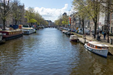 Amsterdam ilkbahar kanalında, teknelerle ve şehrin her iki yakasında da ağaçlar var.