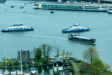 Suyun karşısına bakın, Amsterdam kanalı. A 'dam binasının gözcü kulesinden deniz tankerleri, gemiler ve feribotlar görünüyor.