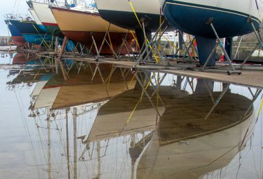 Yağmurdan sonra su birikintilerindeki doğal yansımalarla limandan ayrılan tekneler.