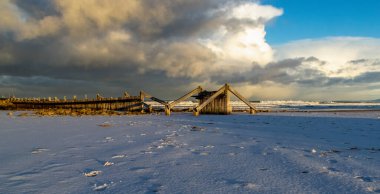 Footprints in the snow on a sandy beach looking to a stormy sky on east beach, Lossiemouth clipart