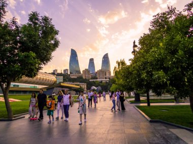 Bakü, Azerbaycan - 23 Temmuz 2023: Denizkenari Milli Parkı 'nda günbatımında, arka planda Alev Kuleleri ile yürüyen insanlar.