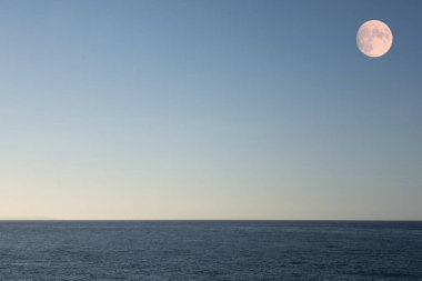 Gün batımında açık gökyüzü ve dolunayı olan deniz ve kopya alanı olarak gökyüzü, arkaplan ya da duvar kağıdı olarak kullan.