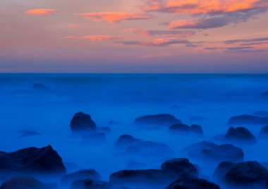 Dalgalar alacakaranlıkta kayalara çarpıyor