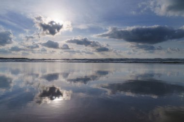 Sahilde gün batımında, güneş bulutların arkasında batar. Deniz kıyısındaki canlı renkleri yansıtır. Donostia-San Sebastian Şehri..