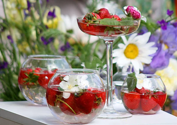 Yaz içecekleri, böğürtlenler ve çilekler yeşil yapraklı ve çiçekler masada çilekli limonata ve taze çilek dolu cam bir kavanozda
