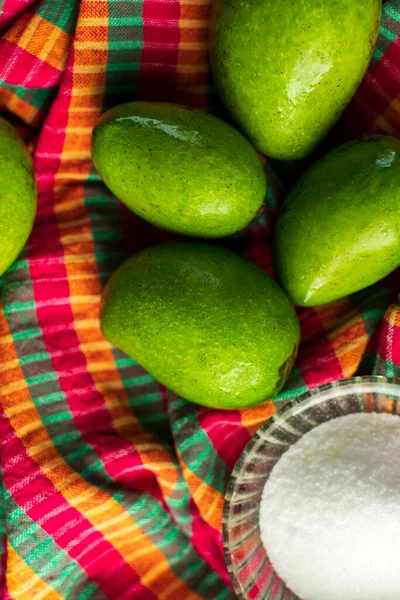 stock image raw green whole mangoes and a glass bowl full of sea salt kept on a kitchen towel selective focus photography with shallow depth of field