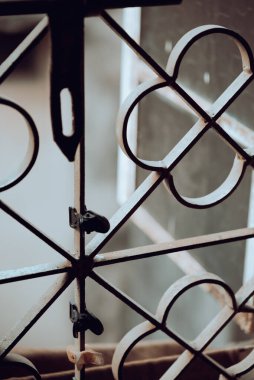 Metal bir kafes yapısını tasvir eden detaylı görüntü, doğal ışıkta ayarlanmış küçük klipsleri içeriyor. Mimari elementleri ve günlük nesnelerle etkileşimlerini, dokuları ve desenleri harmanlamalarını vurgular.