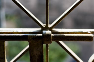 Metal bir kafes yapısını tasvir eden detaylı görüntü, doğal ışıkta ayarlanmış küçük klipsleri içeriyor. Mimari elementleri ve günlük nesnelerle etkileşimlerini, dokuları ve desenleri harmanlamalarını vurgular.