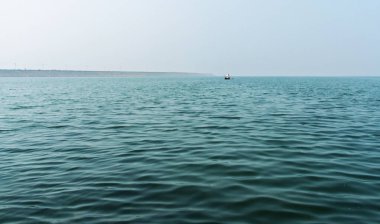 Huzurlu bir okyanus. Dalgalar durmaksızın uzanıyor. Uzaktan görünen küçük bir tekne. Geniş ve berrak bir gökyüzü altında suyun enginliğini gösteren sakin bir manzara..