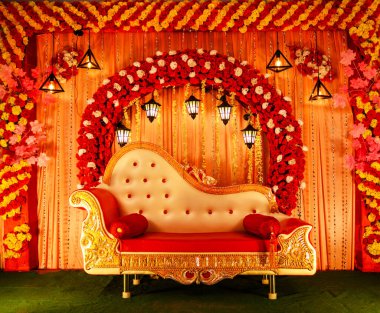 Büyüleyici bir düğün sahnesi tasarımı, canlı çiçekler, güzel süslü bir kanepe, ve sıcak ışıklandırma, özel günler ve kutlamalar için mükemmel bir atmosfer hazırlıyor..